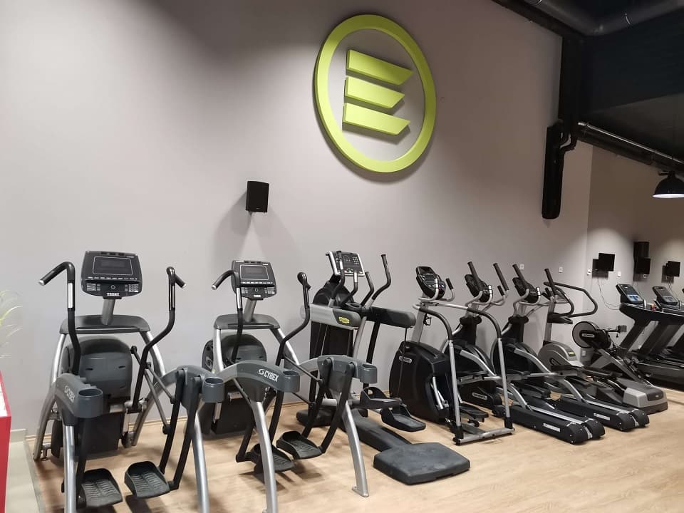 A falon az Elite Fitness zöld logója, előtte ellipszistréner-gépek sora